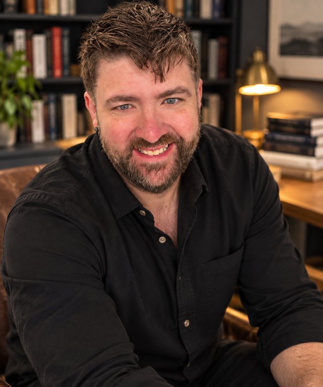 Christopher Fenimore, smiling, seated in front of a wall of bookshelves